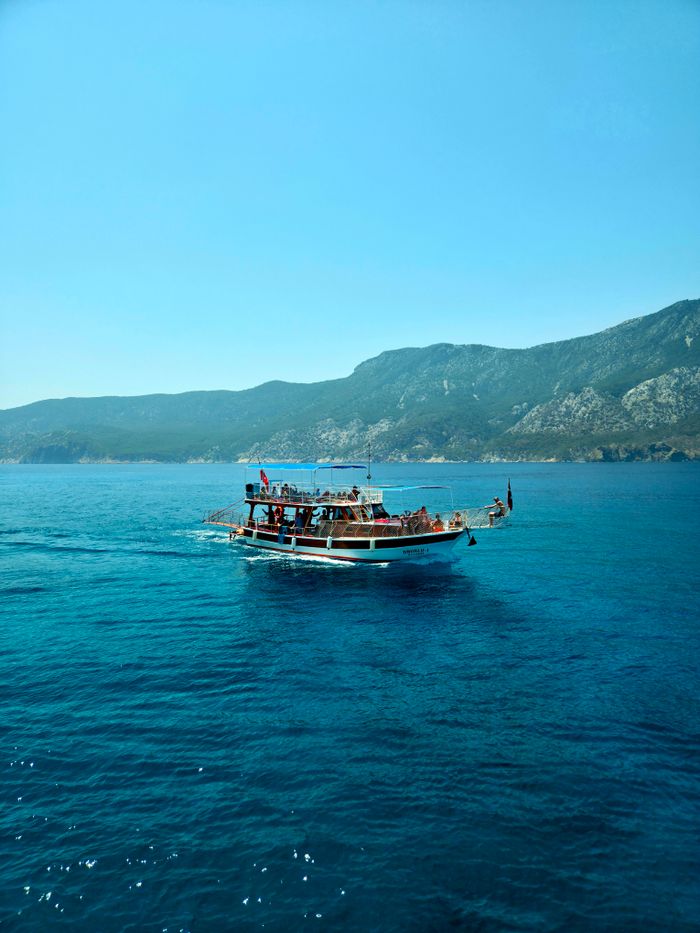 A boat with passengers navigates the clear blue waters off Antalya, Türkiye, with a mountainous backdrop.